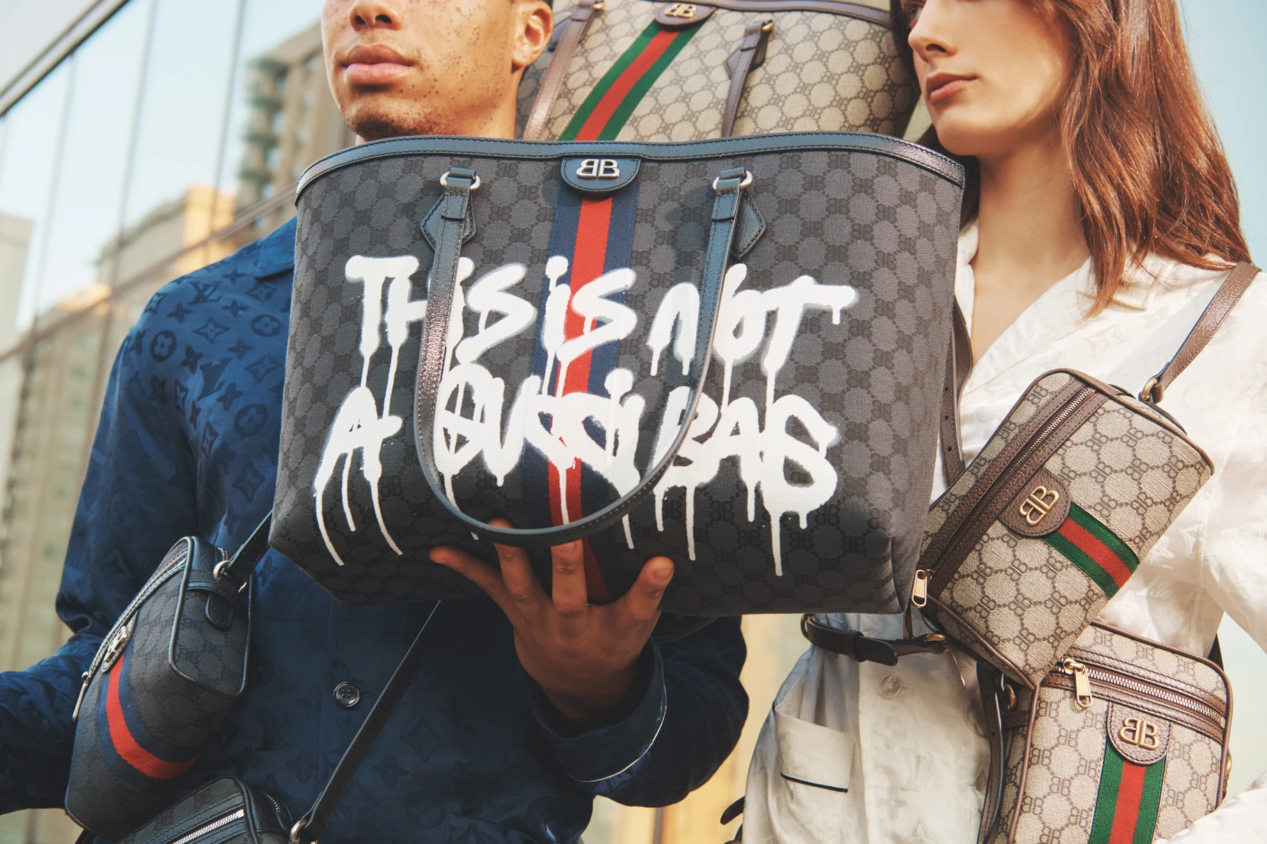 Model holds the Gucci x Balenciaga Hacker Project tote spray-painted This Is Not A Gucci Bag, GG and BB monograms surrounding it